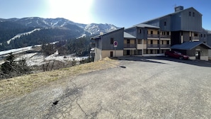 A multi-story building with a parking area and a view of snow-capped mountains. - T2 avec une vue imprenable sur la station du Liora (Le Lioran)