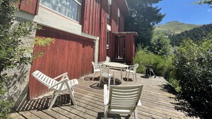 A wooden deck with white plastic chairs, a table, and a small barbecue grill. - Chalet les Digitales - Rocher du cerf (Le Lioran)