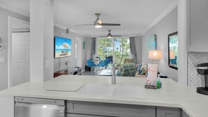 A modern kitchen with a dishwasher, a ceiling fan, and a dining area with blue chairs and a table.