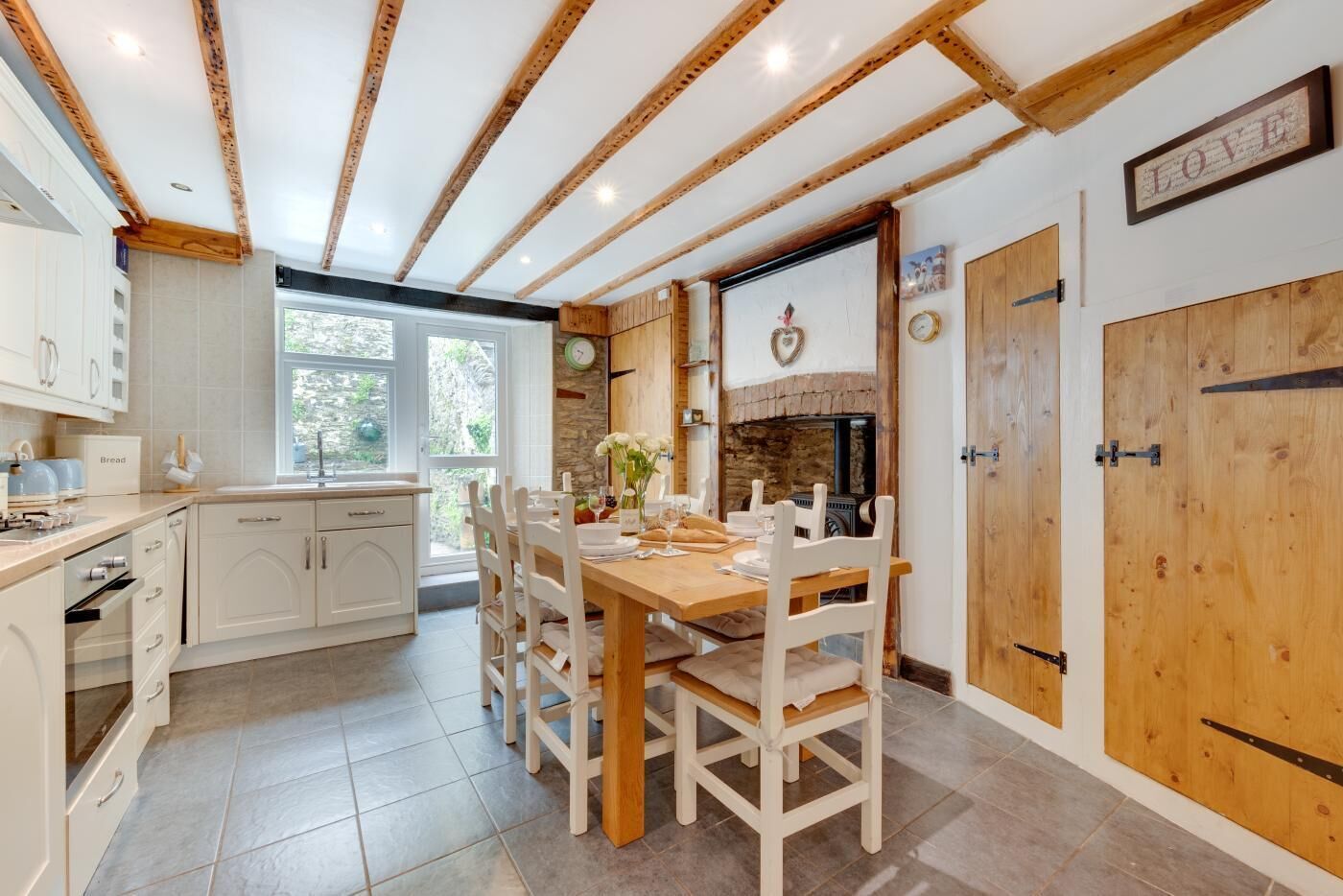 A modern kitchen with white cabinetry, a wooden dining table, and a stone fireplace.