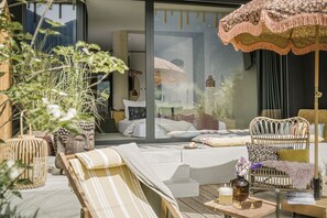 A sunlit outdoor seating area with a sofa, chairs, and a table, surrounded by potted plants and a large umbrella. - Coolnest (Ramsau im Zillertal)