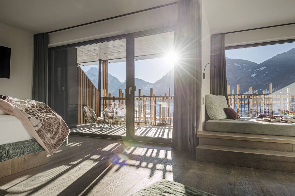 Ein modernes Hotelzimmer mit einer großen Schiebeglastür, die auf einen Balkon mit Bergblick führt.