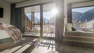 Une chambre d’hôtel moderne dotée d’une grande porte-fenêtre coulissante donnant sur un balcon avec vue sur les montagnes.