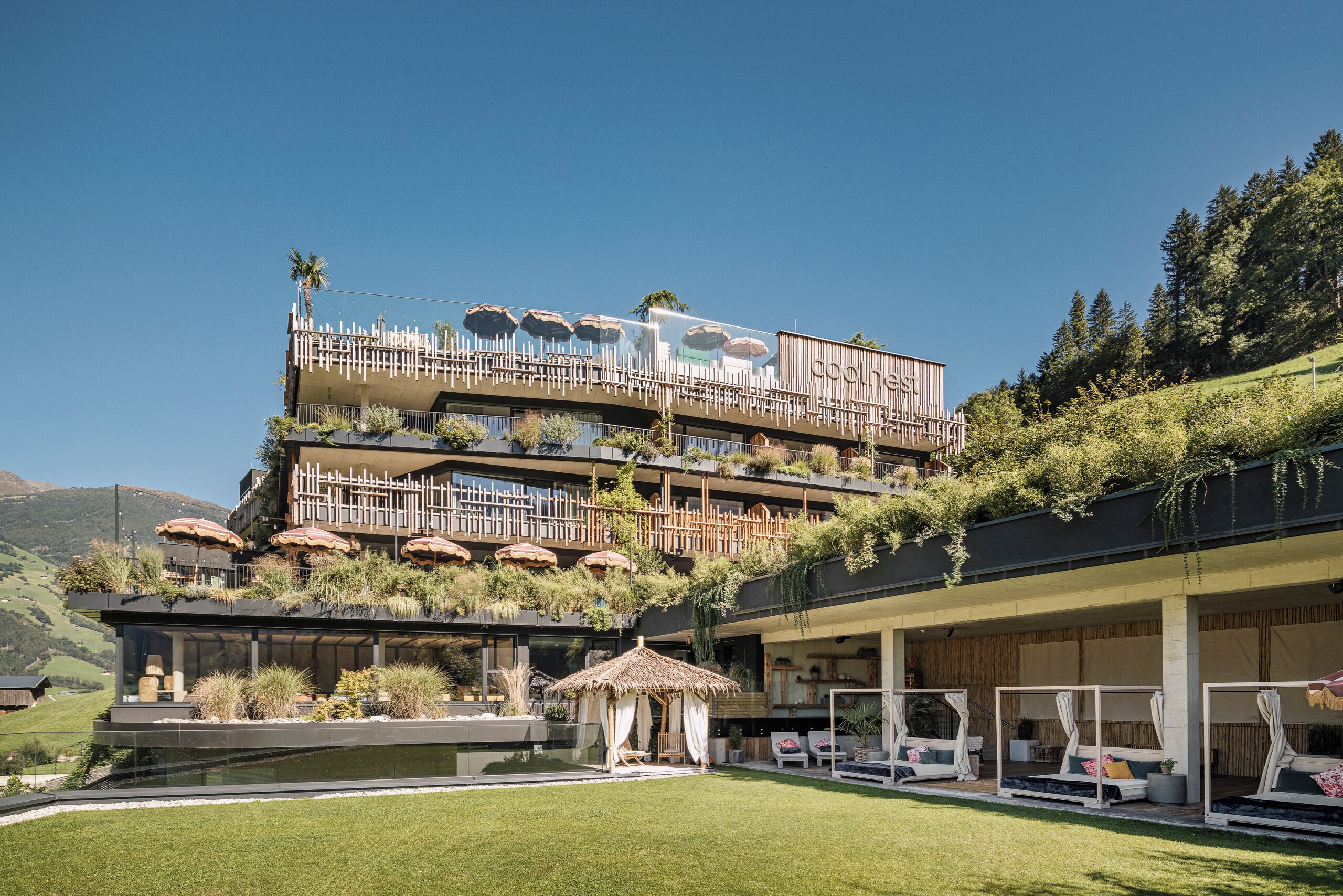 A multi-story hotel with outdoor seating, a pool, and a view of the surrounding hills.