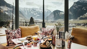 Una mesa de comedor con alimentos para el desayuno, un florero con flores y vistas a montañas nevadas.
