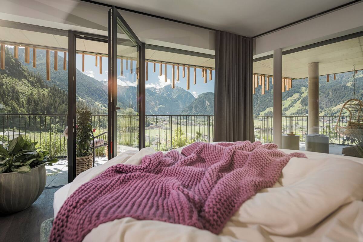 Ein Schlafzimmer mit einem großen Bett, Bergblick und einem Balkon mit Pflanzen.