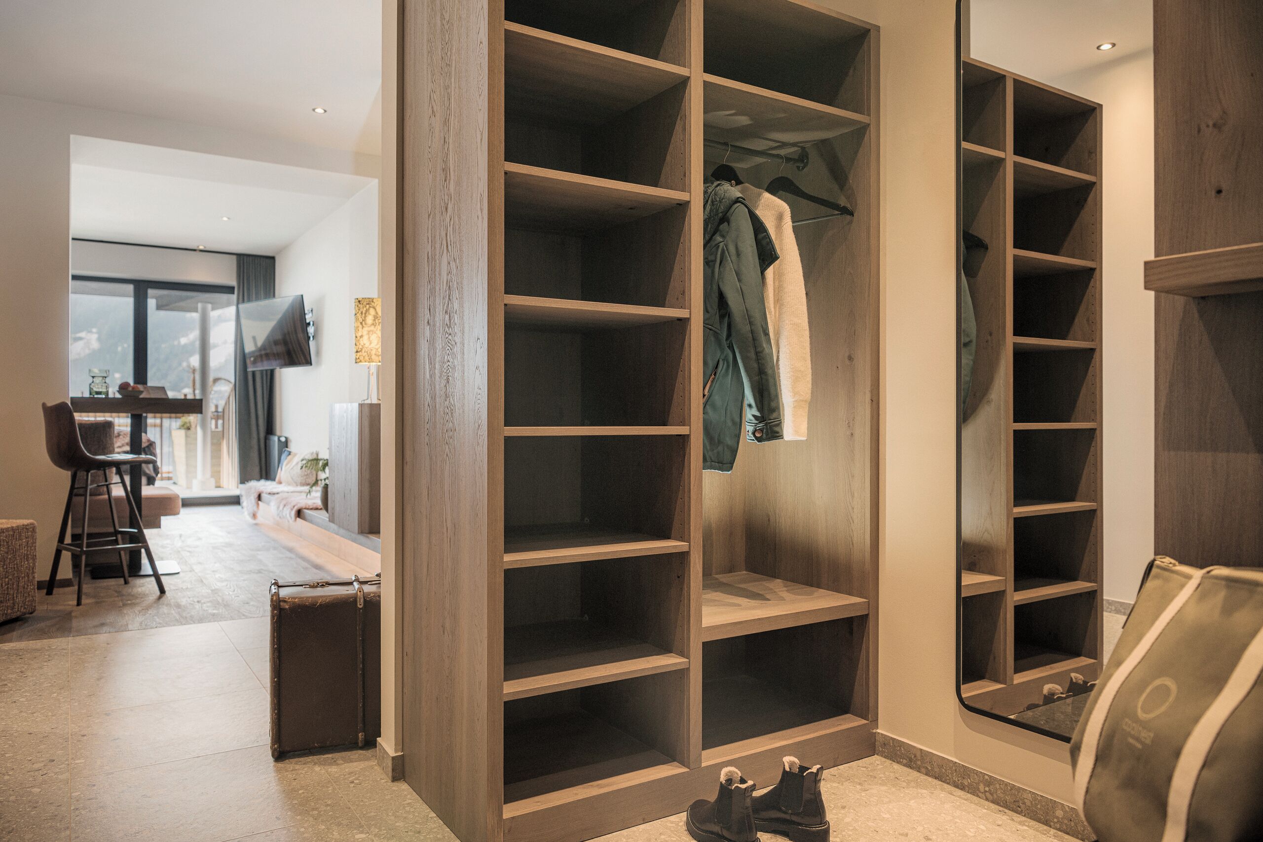 A spacious walk-in closet with multiple shelves and hanging space, a seating area with a table and chairs, and a view of a cityscape through a large window.