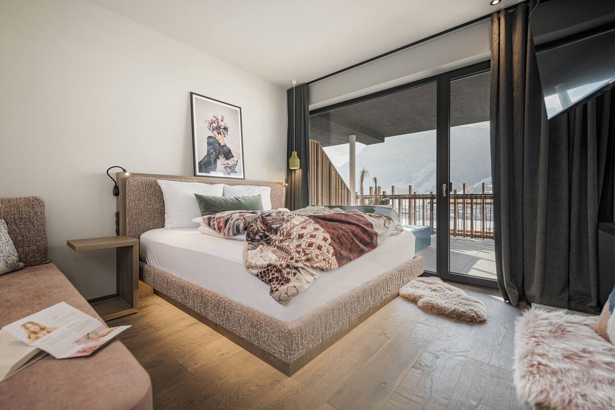 Ein modernes Schlafzimmer mit einem großen Bett, einem Nachttisch, einer Leseecke und einem Balkon mit Blick.
