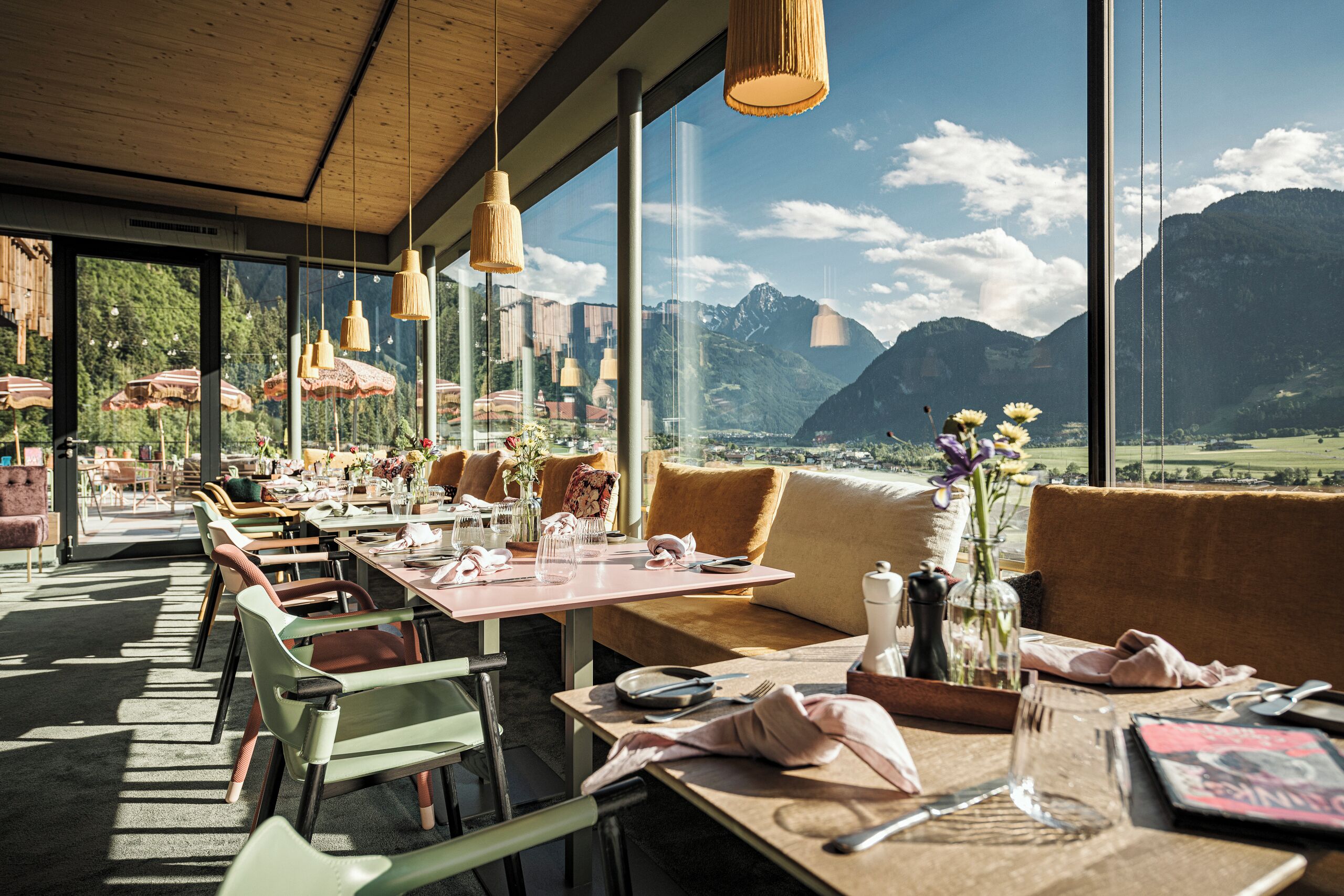 Un restaurante con mesas dispuestas para comer, ventanas amplias con vistas a la montaña y lámparas colgantes.