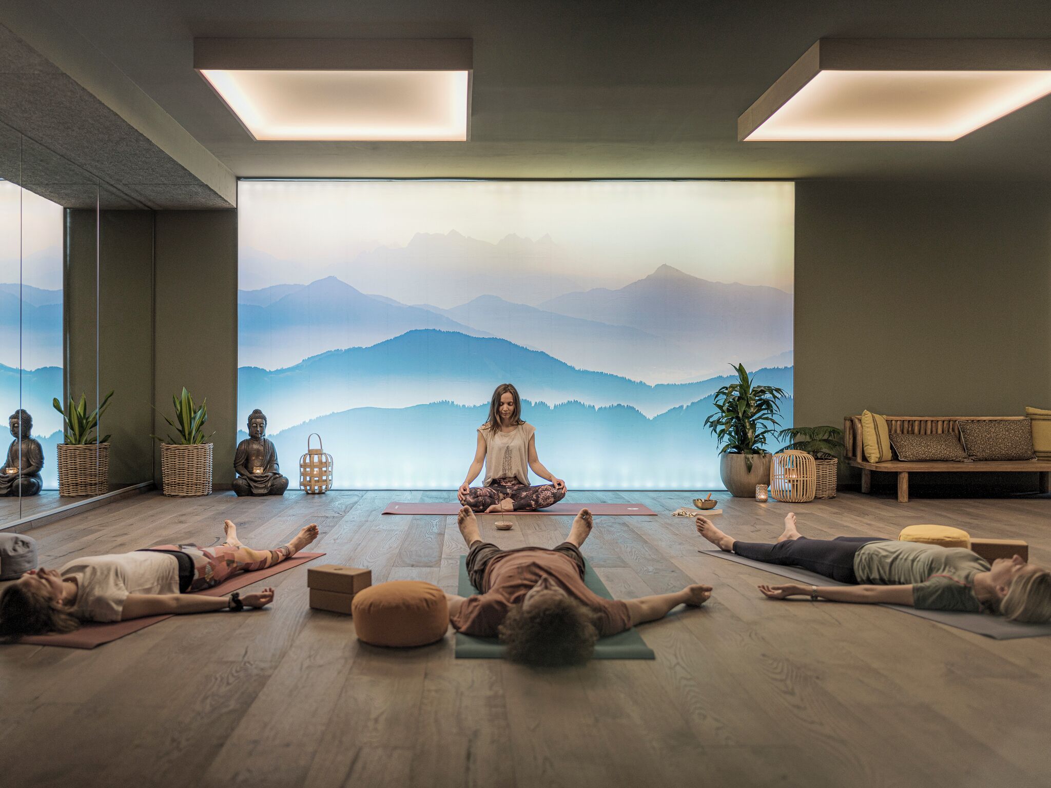 Un cours de yoga dans une salle dotée d’un plancher en bois, d’une grande fresque représentant des montagnes et d’un canapé.