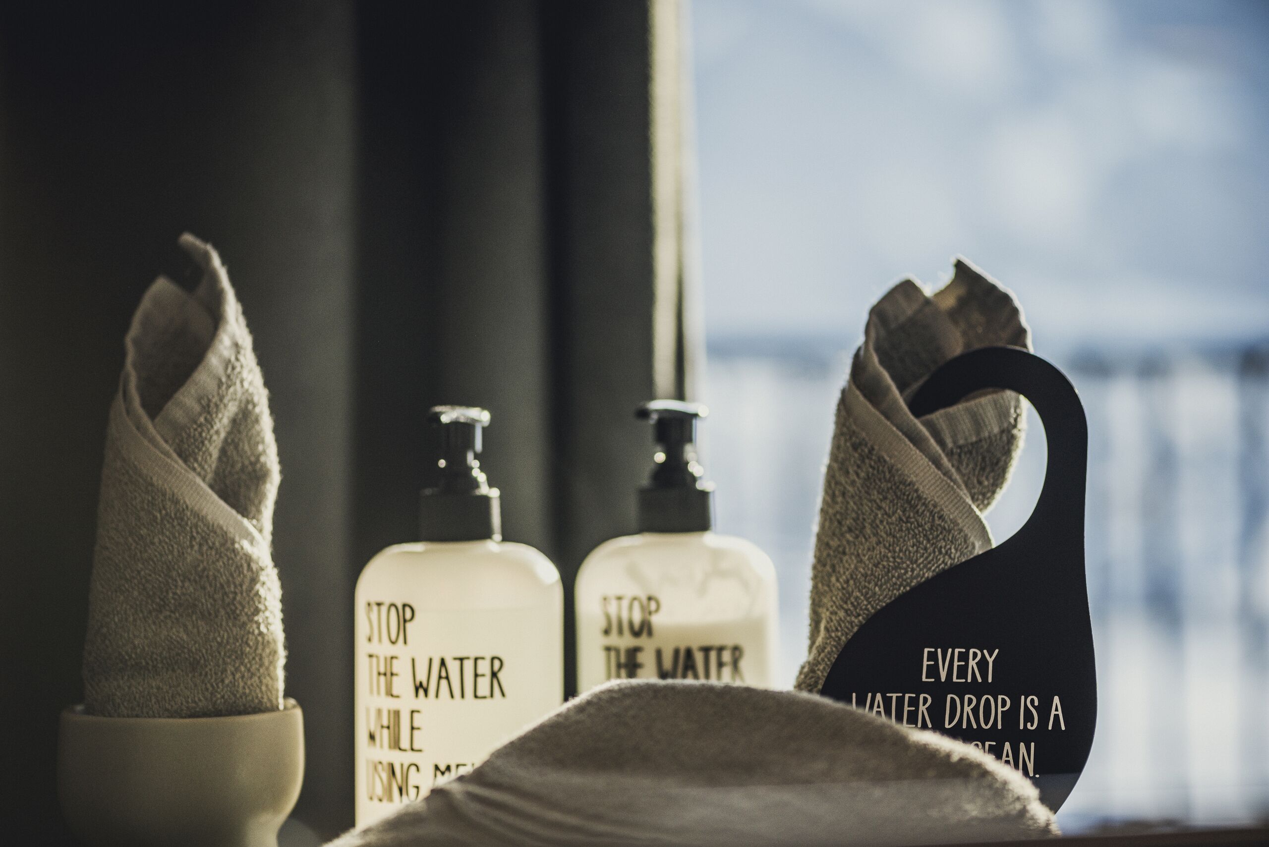 Une salle de bain équipée de serviettes, d’un distributeur de savon et d’une affiche sur la nécessité d’économiser l’eau.