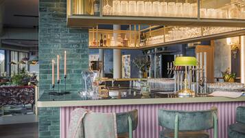 A bar area with a green-tiled counter, bar stools, and a mirrored wall displaying glasses and bottles.