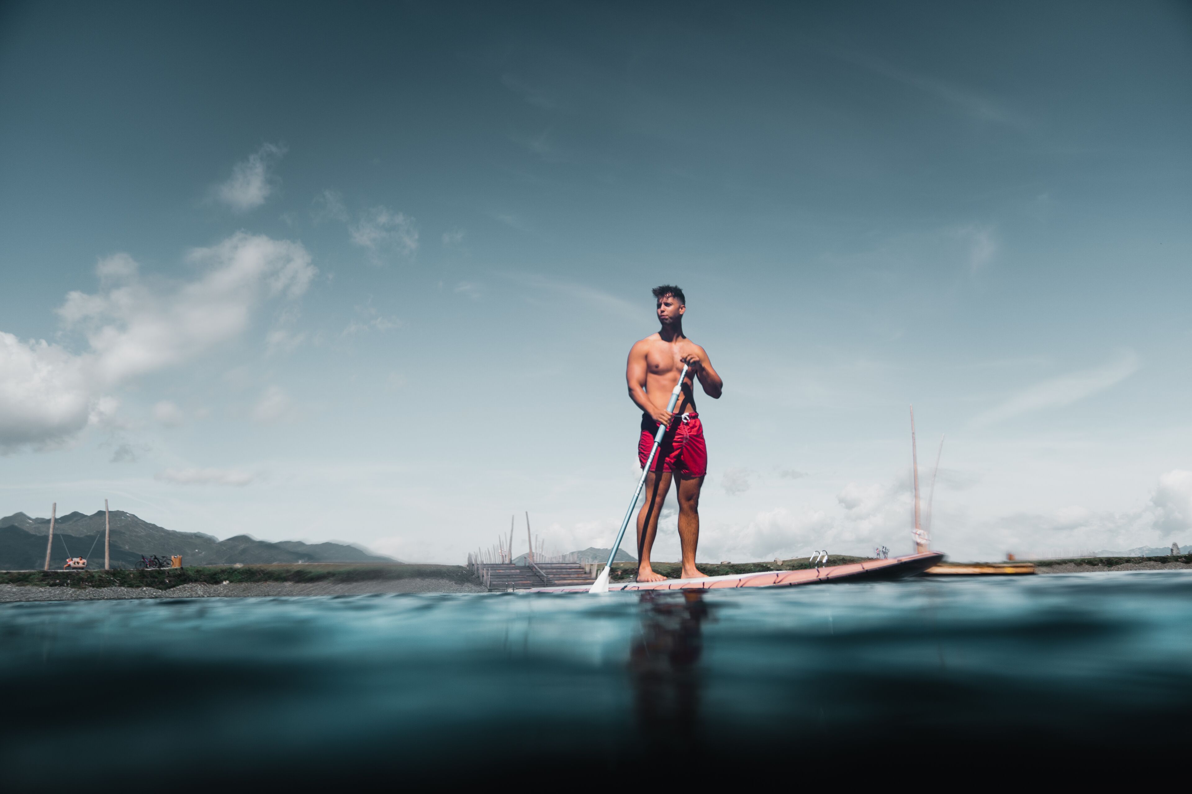 En person står på et paddleboard i vandet, med en klar himmel og fjerne bjerge.