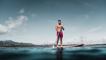 En person står på et paddleboard i vandet, med en klar himmel og fjerne bjerge.