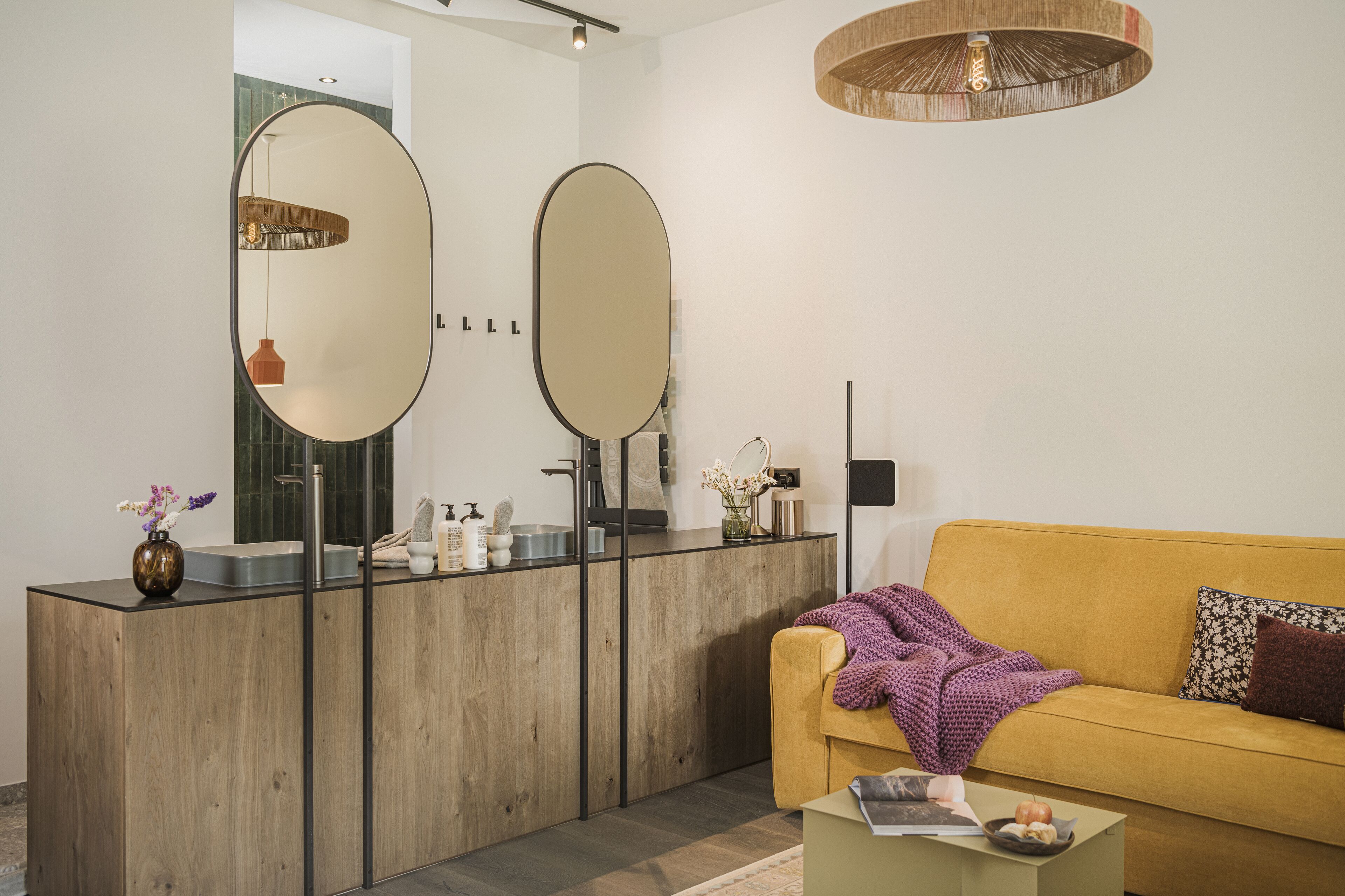 Un baño moderno con tocador de madera, dos espejos, un lavamanos y un sofá amarillo en el área de estar contigua.
