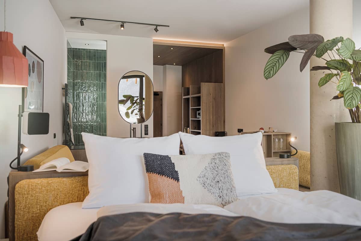 Ein modernes Schlafzimmer mit Bett, Nachttischen, einem Spiegel und einer Pflanze.