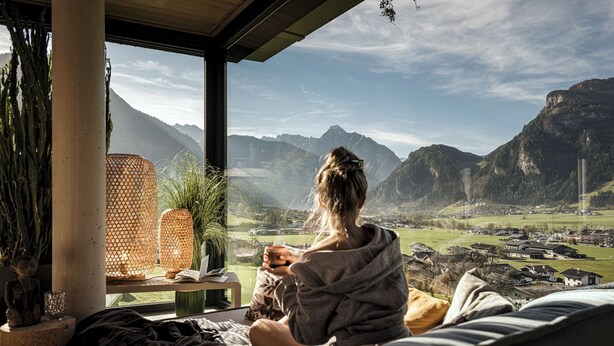 Una persona sentada en una cama con vistas a la montaña a través de una ventana.