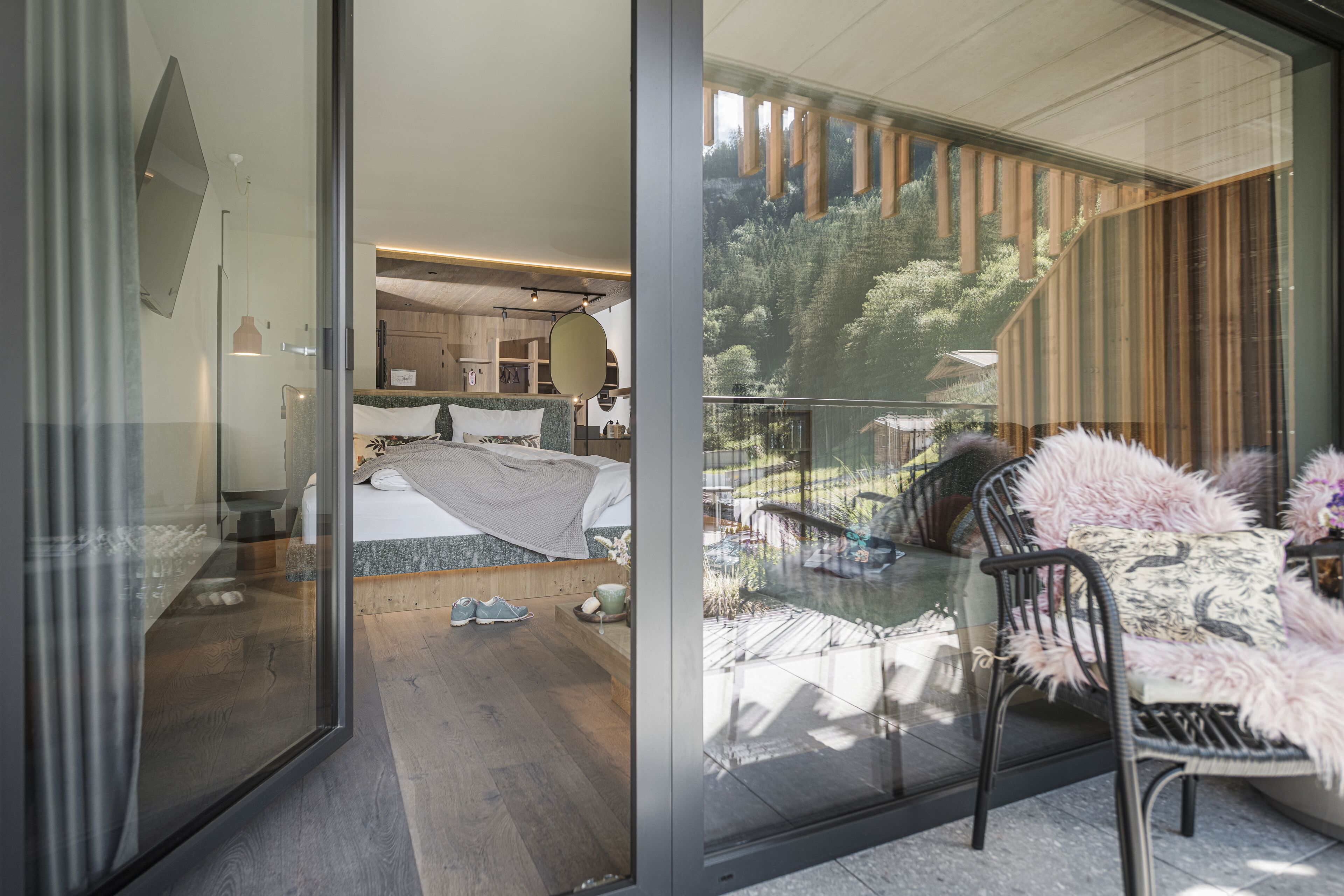 Une chambre moderne avec un grand lit, une porte vitrée donnant sur un balcon avec vue sur les arbres et une terrasse en bois.