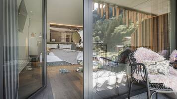Une chambre moderne avec un grand lit, une porte vitrée donnant sur un balcon avec vue sur les arbres et une terrasse en bois.