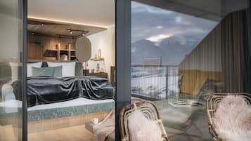 A modern bedroom with a large bed, a glass wall, and a view of mountains.