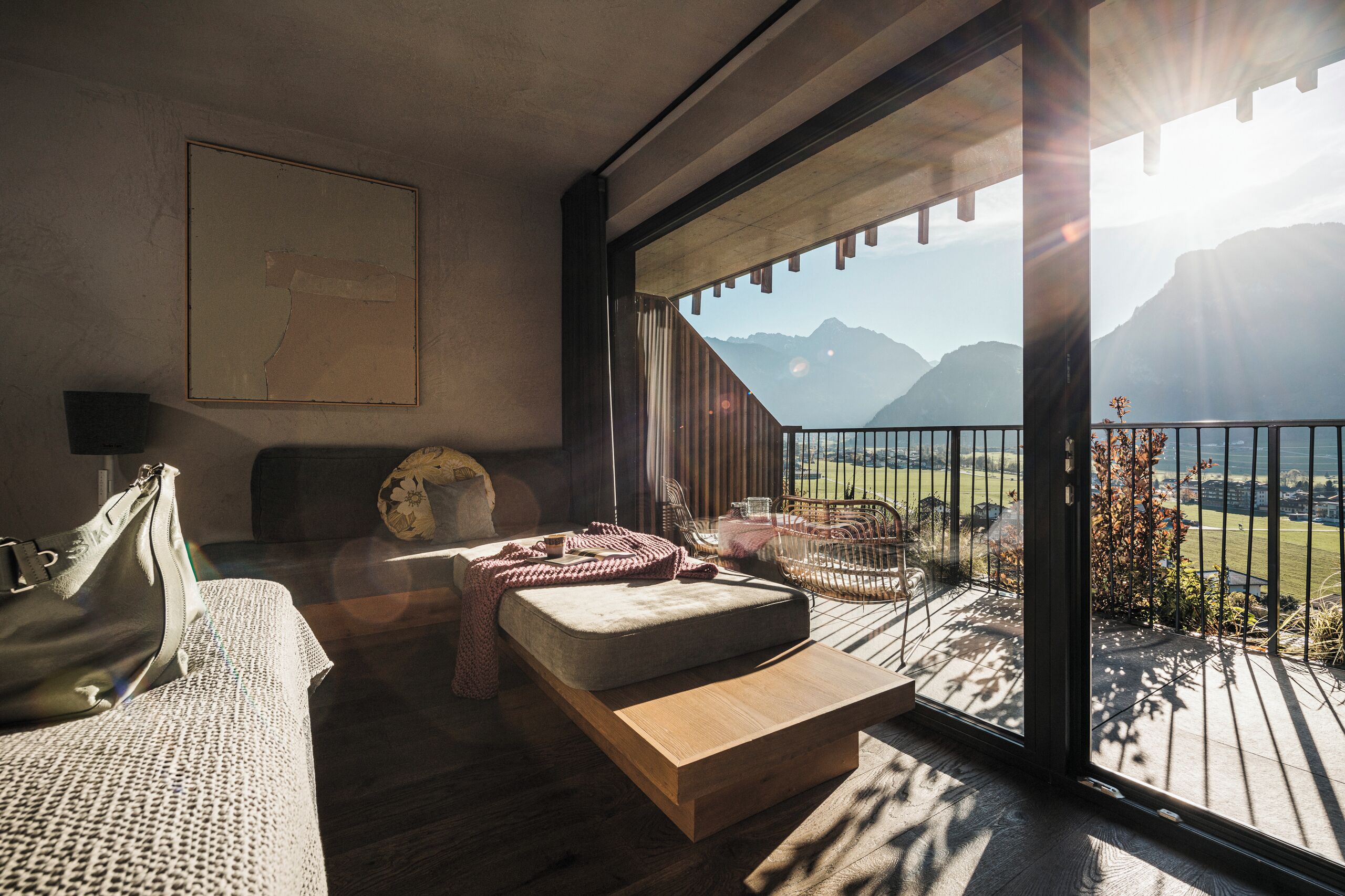 A modern room with a large window overlooking mountains, a sofa, a wooden table, and a view of the outdoors.