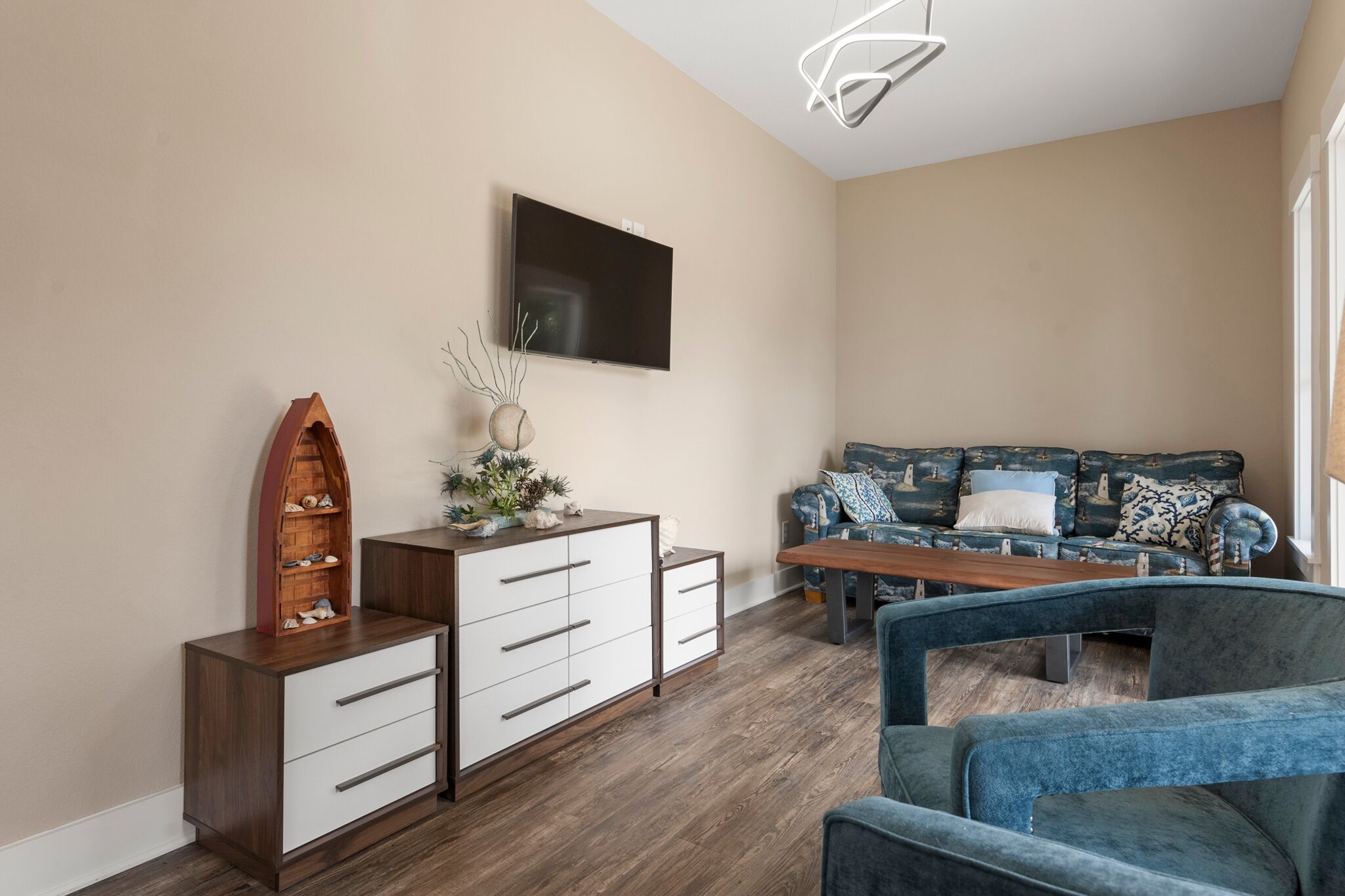 Ein modernes Wohnzimmer mit einem Holzschrank, einem Flachbildfernseher, einer Couch mit gemusterten Kissen und einem Couchtisch.