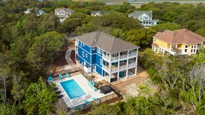 A large two-story house with a swimming pool, surrounded by dense trees and a view of the ocean. - All Inn and Then Some: Pool, Spa, Theater Room (Corolla)