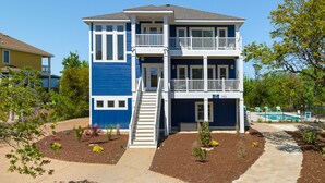 A two-story house with a balcony, a front yard with landscaping, and a visible address number. - All Inn and Then Some: Pool, Spa, Theater Room (Corolla)