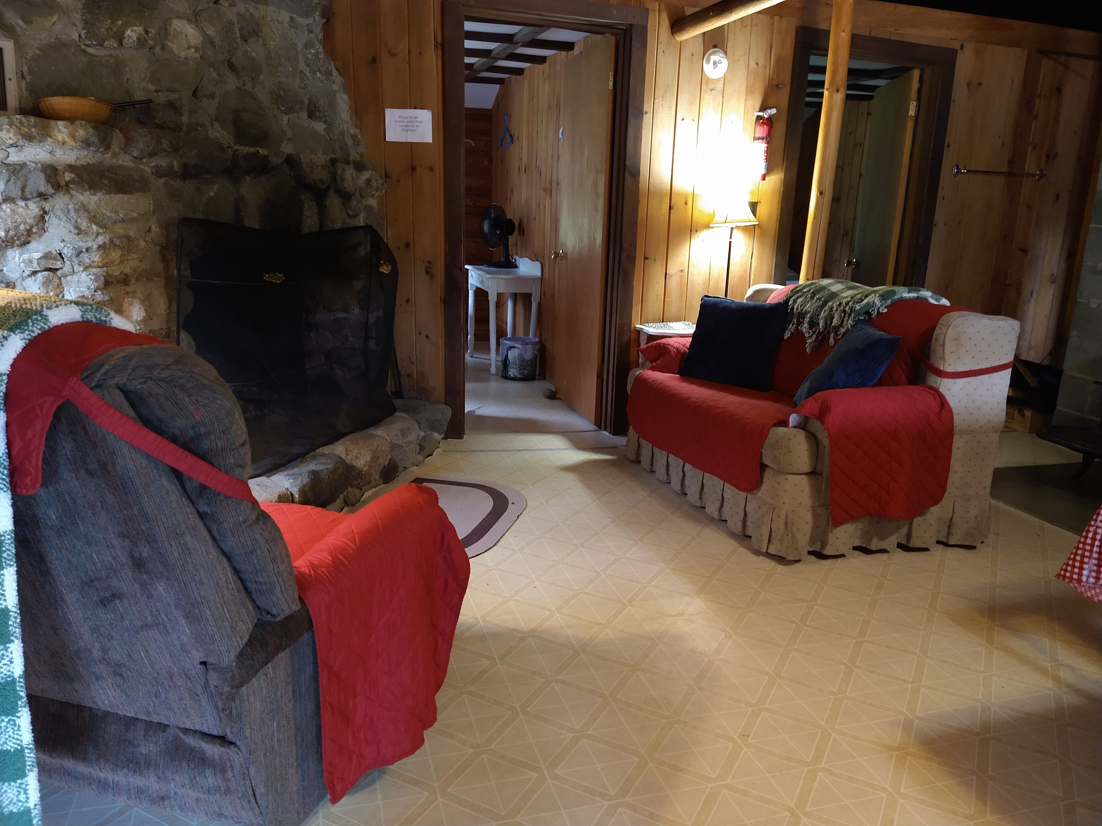 A cozy room with a stone fireplace, wooden walls, and a sofa with red blankets.