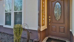 A brown front door with a welcome sign, a window with blinds, and a small tree in the foreground. - The Sweet Home! Minutes from Mall of GA and Suwannee! (Sugar Hill)