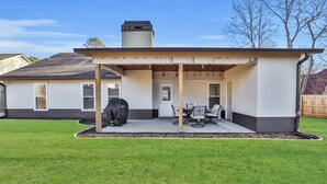 A covered patio area with a barbecue grill, outdoor seating, and a chimney. - The Sweet Home! Minutes from Mall of GA and Suwannee! (Sugar Hill)