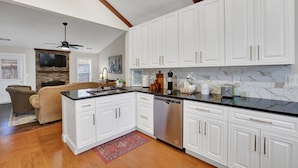 A modern kitchen with white cabinetry, a black countertop, and a dishwasher. There is a wooden ceiling beam and a ceiling fan. - The Sweet Home! Minutes from Mall of GA and Suwannee! (Sugar Hill)