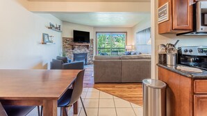 Una cocina moderna con comedor, chimenea de piedra y un amplio ventanal con vistas a un paisaje verde.
