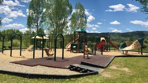 Un parque infantil con columpios, toboganes y estructuras para escalar, rodeado de árboles y un cielo despejado.