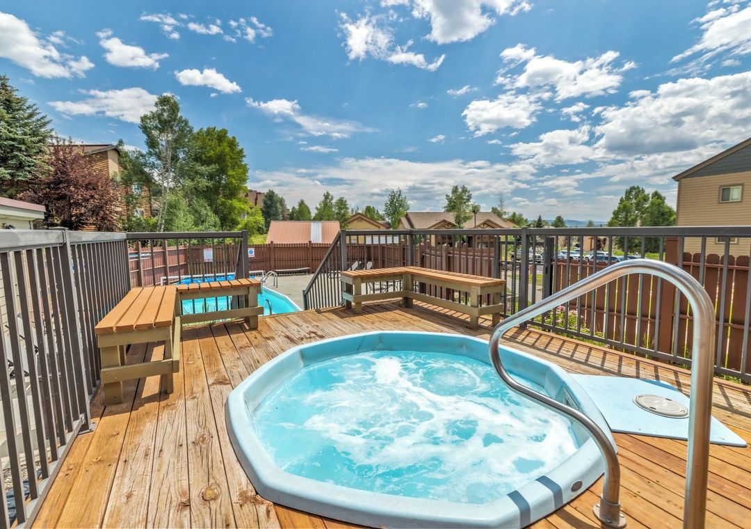 A wooden deck with a hot tub, a pool, and a wooden bench.