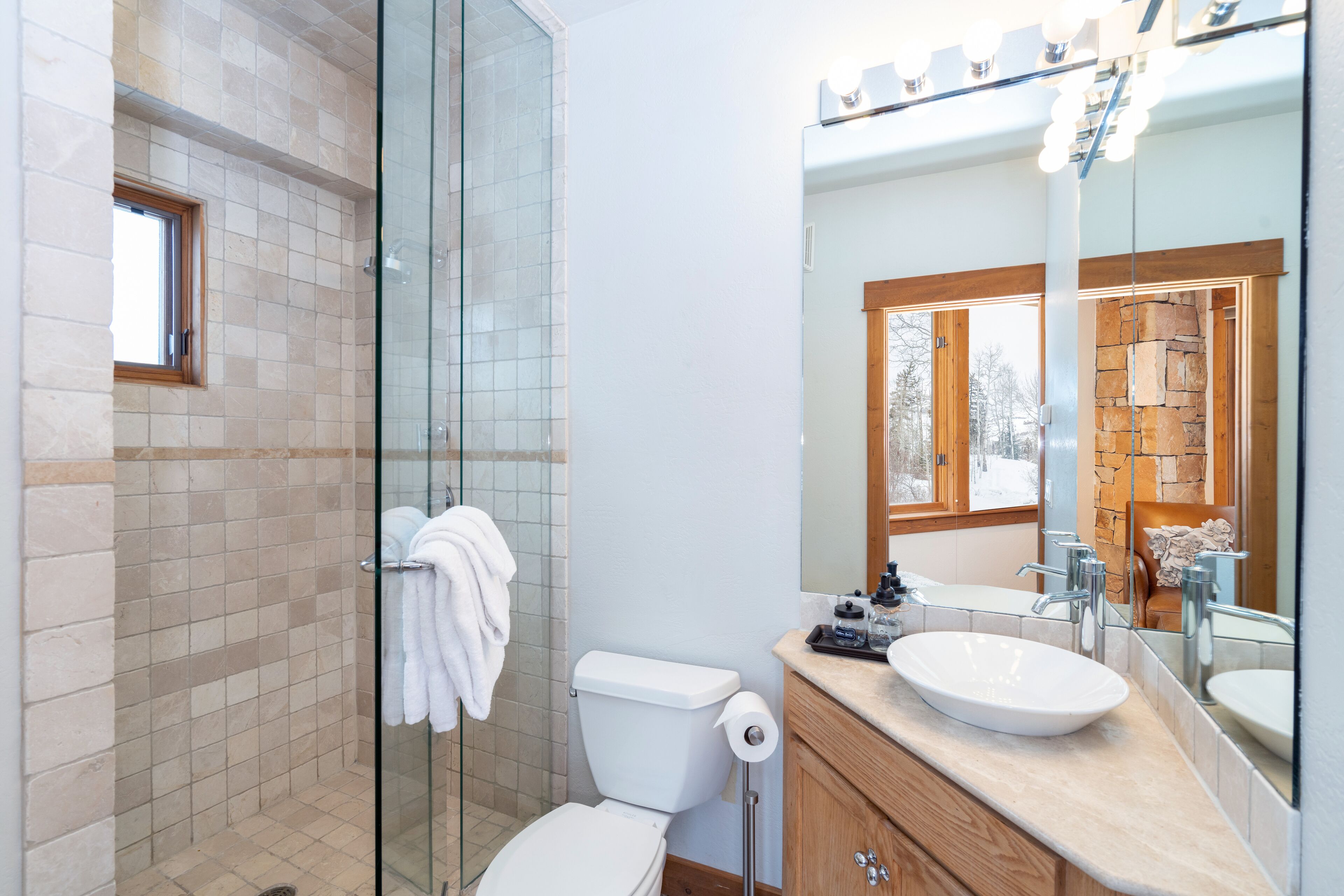 Un bagno moderno con cabina doccia in vetro, un water bianco, un lavabo con specchio e mobili contenitori in legno.