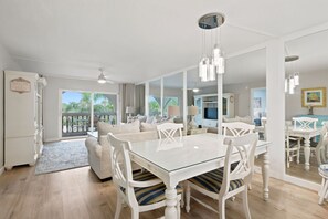 A modern living room with a glass dining table, white furniture, and a view to the outside.