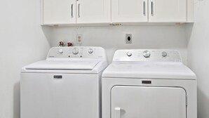A laundry room with two white front-loading washing machines and a set of white cabinets above. - Breakers West B3 | Stunning and Spacious West Gulf Drive Residence | Steps to Beach (Sanibel)