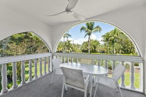 A covered outdoor area with a table and chairs, a ceiling fan, and a view of palm trees and greenery. - Breakers West B3- Stunning and Spacious West Gulf Drive Residence (Sanibel)