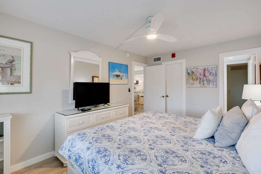 Ein Schlafzimmer mit einem Bett, einem Fernseher, einem Deckenventilator und Kunstwerken an den Wänden.