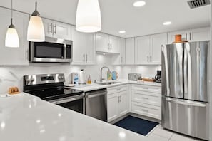 A modern kitchen with white cabinets, stainless steel appliances, and pendant lighting.