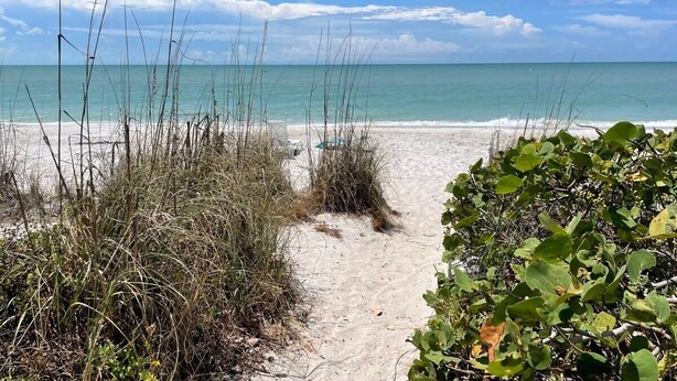 A sandy beach path leading to the ocean with sparse vegetation. - Breakers West B3 | Stunning and Spacious West Gulf Drive Residence | Steps to Beach (Sanibel)