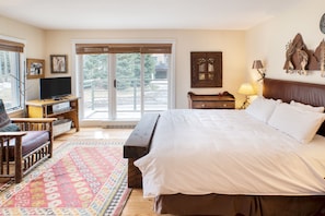 A bedroom with a large bed, a wooden bench, a television, and a view through a sliding glass door. - Blue Mesa Lodge 23C by AvantStay | Functional Ski In/Ski Out Studio w/ Balcony (Telluride)