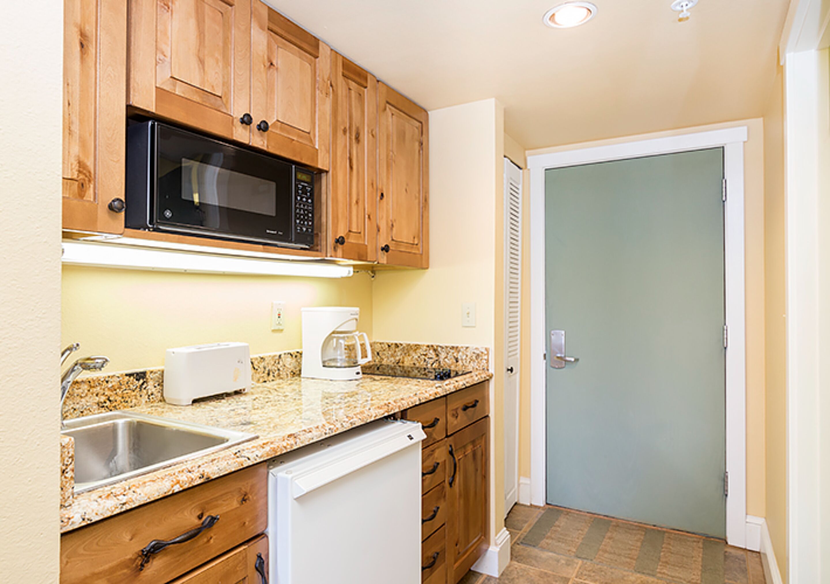 A compact kitchen with wooden cabinets, a microwave, a toaster, and a coffee maker.