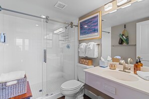 Ein modernes Badezimmer mit einer Duschkabine aus Glas, einer weißen Toilette, einem Waschbecken mit Spiegel und einem gerahmten Bild an der Wand.