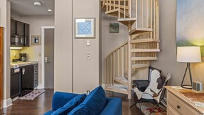 Ein modernes Wohnzimmer mit einem blauen Sofa, einer Wendeltreppe aus Holz und einer Küche im Hintergrund.