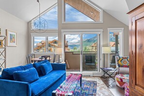 A spacious living area with a blue sofa, a colorful rug, and a view of a mountain landscape through large windows. - Blue Mesa Lodge 40A by AvantStay | Ski In/ Ski Out Unit w/ Balcony! (Telluride)