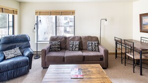 Una sala de estar con un sofá marrón, un sillón de cuero negro, una mesa de centro de madera y una mesa de comedor con sillas.