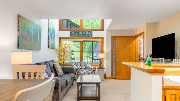 A cozy living room with a sofa, coffee table, and a dining table. There is a sign above the windows that reads "The Gathering Place." - Cimarron Lodge 14 by AvantStay | Ski-In/Ski-Out Property w/ Two Hot Tubs! (Telluride)