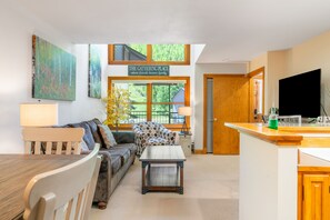 A cozy living room with a sofa, coffee table, and a dining table. There is a sign above the windows that reads "The Gathering Place." - Cimarron Lodge 14 by AvantStay | Ski-In/Ski-Out Property w/ Two Hot Tubs! (Telluride)